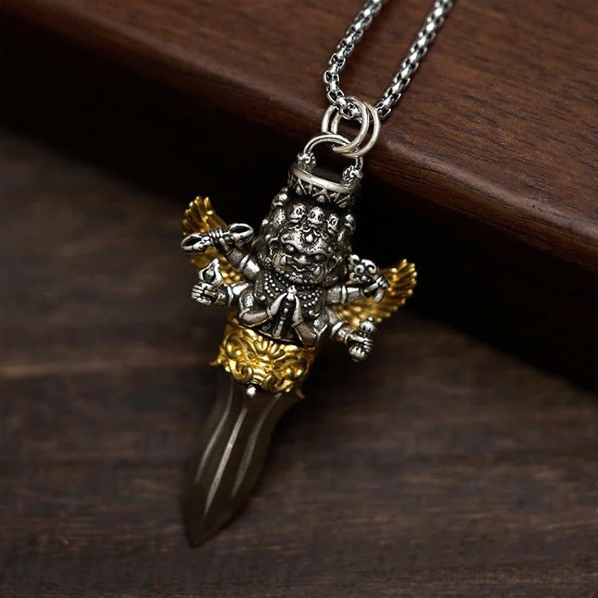 Buddhist vajra pendant necklace in antique silver and gold tone, overhead view on wooden board background showcasing winged protector design and carved decorative base