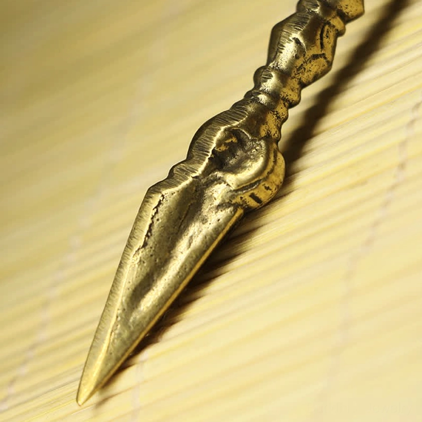 Close-up detail of copper vajra dorje featuring bright golden brass finish with carved deity figure on handle and ridged nine-pronged shaft