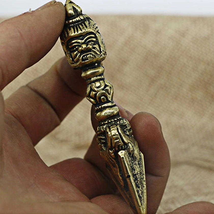 Close-up hand-held copper vajra dorje showing sharp pointed blade and detailed craftsmanship for meditation practice