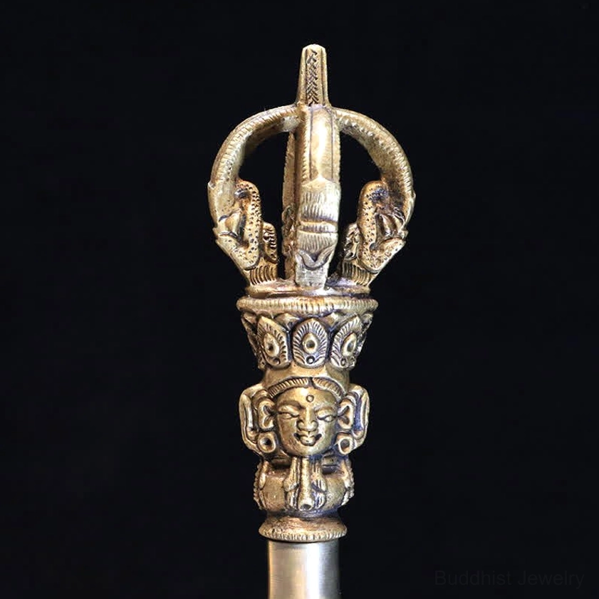 Close-up of polished copper five-pronged vajra dorje with detailed Buddha head carving on pure black background