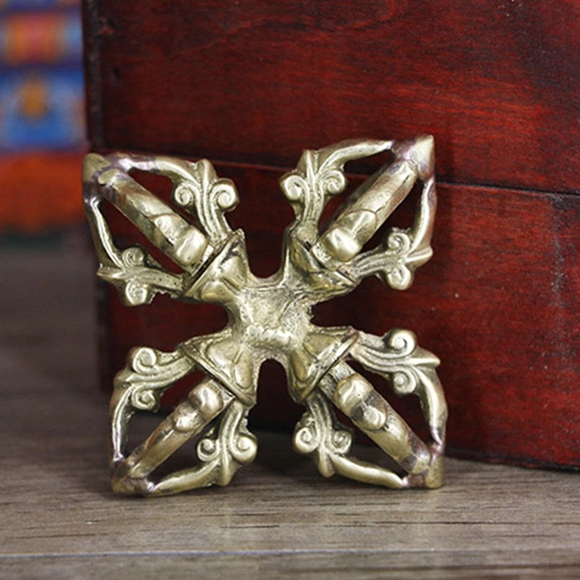 Copper vajra front three-quarter angle against red wooden box with symmetrical hollowed metal structure and aged brass color
