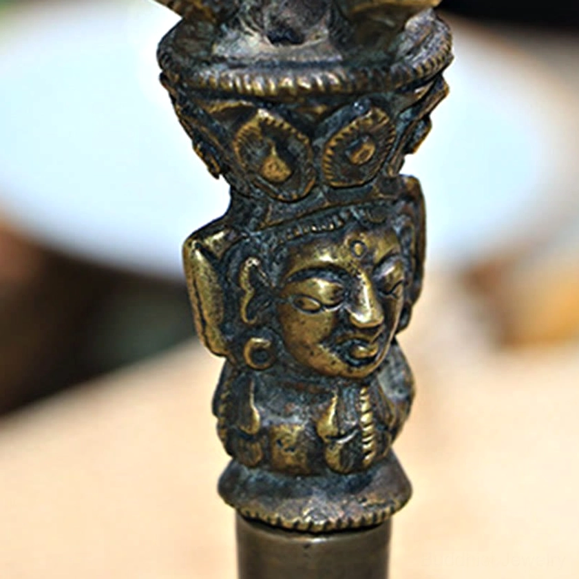 Macro close-up of vajra handle showing intricate carved Buddha face and decorative religious patterns in detail