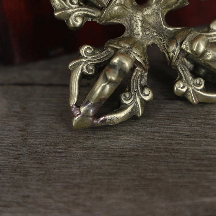Extreme close-up of copper vajra prongs showing aged brass metal wear and decorative scroll details