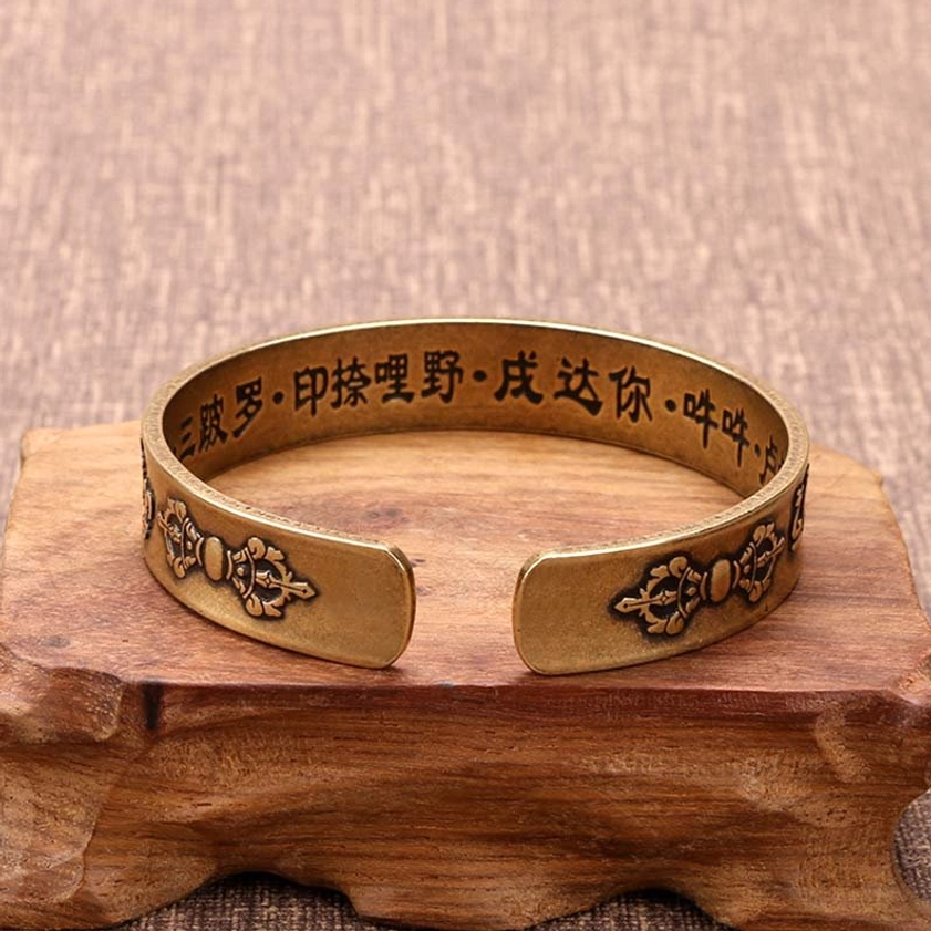 Overhead view of Vajra symbol copper cuff bracelet with engraved mantras on wooden display stand