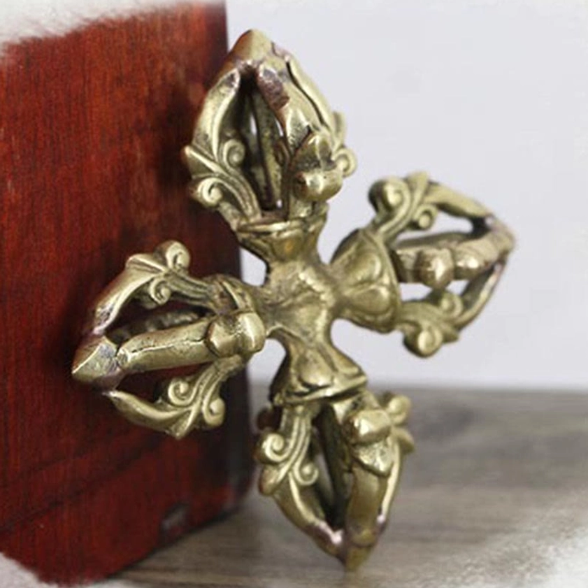 Copper double dorje three-quarter side view leaning against red wooden box with symmetrical four-pronged hollowed design