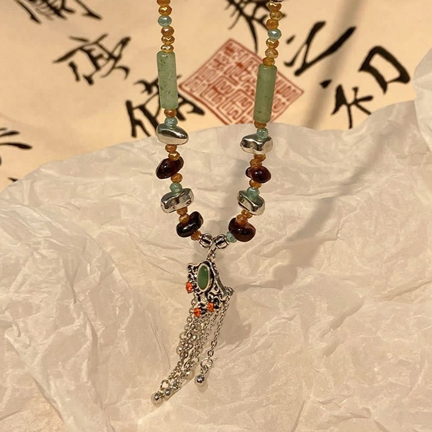 Close-up flat lay view of vintage inspired beaded tassel necklace featuring green tube beads, dark brown stones, and silver charm on Asian calligraphy background