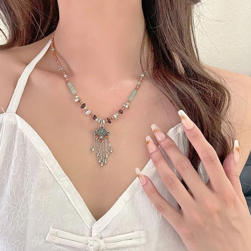 Vintage spiritual tassel necklace displayed on neck showing mixed colored beads, silver tassel with green enamel inlay, and adjustable chain extender for comfort