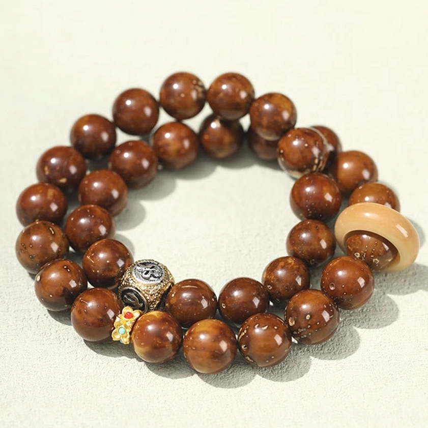 Buddhist double wrap bracelet with purple gold rat seeds showing engraved metal charm and gemstone decoration