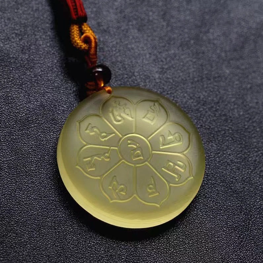 Close-up detail of eight-petal Liuli crystal pendant with engraved mantra patterns and light yellow finish