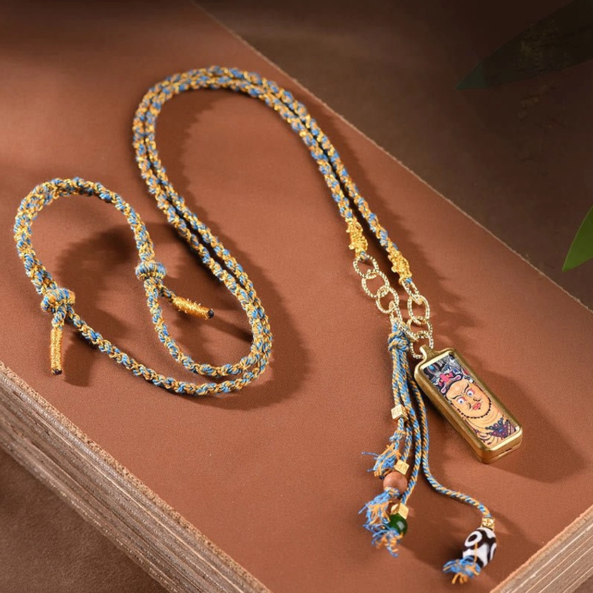Flat lay of thangka pendant necklace with braided cord chain and tassel bead decorations on book background