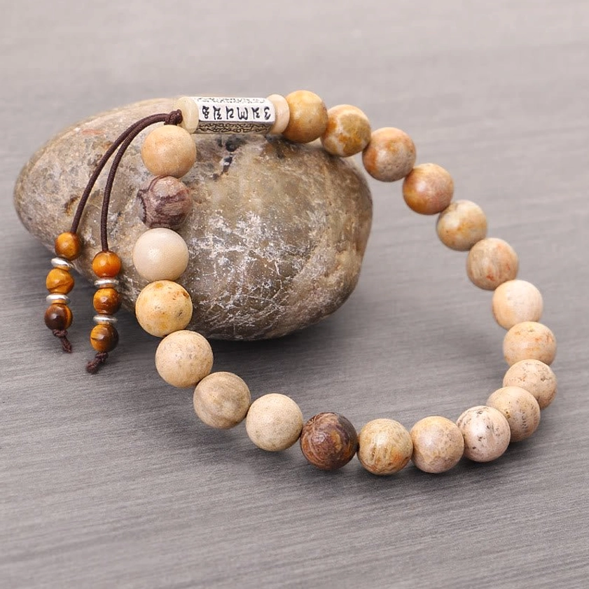 Side angle view of weathered stone Buddhist bracelet with silver mantra charm and natural beads on river stone