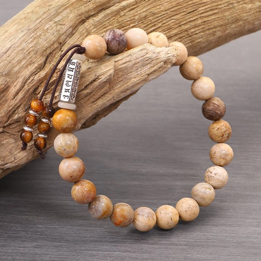 Weathered stone Om Mani Padme Hum bracelet displayed on natural driftwood with mantra charm and tassel detail