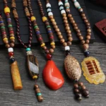 Collection of handmade Wenge wood Bodhi seed necklaces with colorful agate beads and Buddhist pendants displayed on dark wooden surface