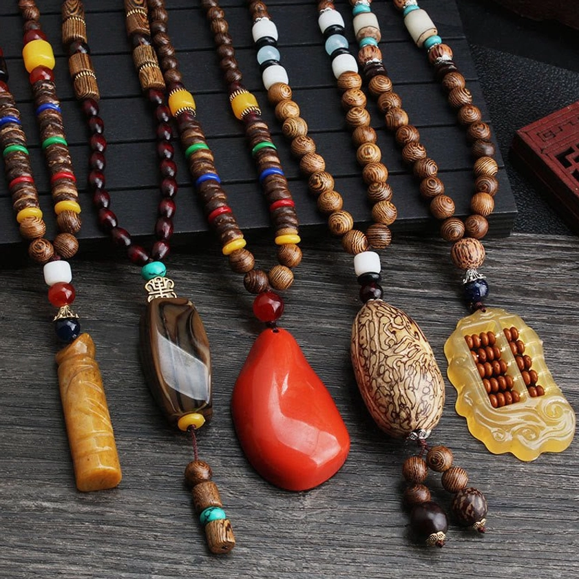 Collection of handmade Wenge wood Bodhi seed necklaces with colorful agate beads and Buddhist pendants displayed on dark wooden surface