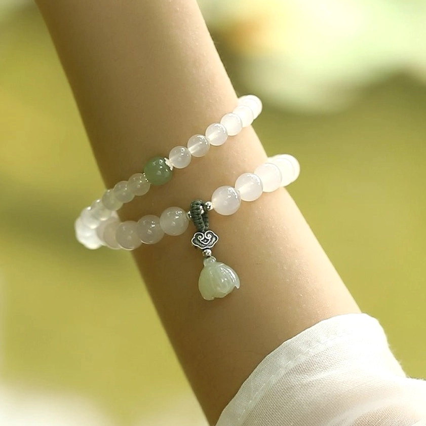 Frosted white agate beads with pale green jade spacer and carved lotus pendant worn on wrist close-up