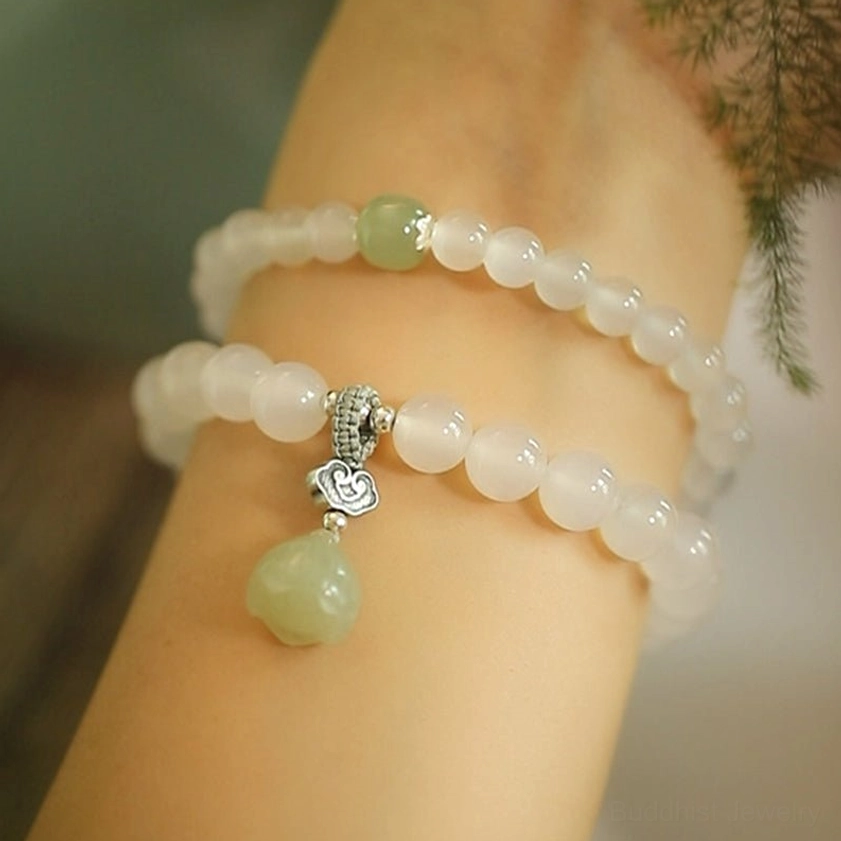 Double-layer white agate bracelet with pale green jade spacer and large carved lotus pendant on arm outdoor setting