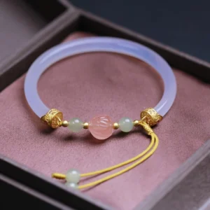 White agate lotus bead Buddhist bracelet with jade accents and gold plating, displayed on purple jewelry tray with tassel charm