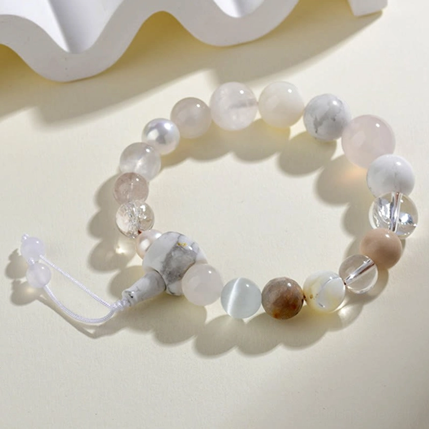 Flat lay top view of white agate pearl balance clarity bracelet with adjustable tassel on beige background