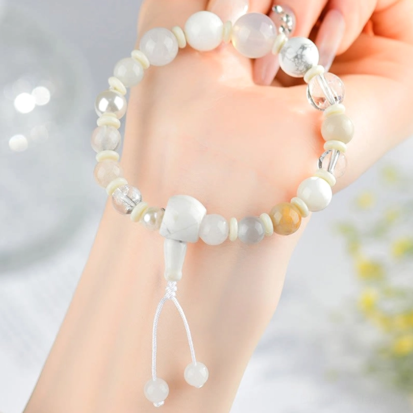 White agate pearl bracelet worn on left hand with dangling tassel and floral background