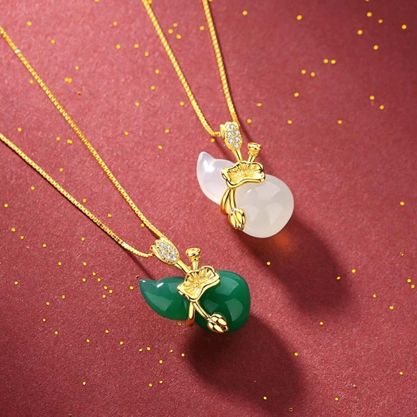 Two jade gourd pendant necklaces flat lay - cyan jade and white jade versions with adjustable gold chains on red background