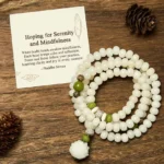 White Bodhi lotus mala beads with green accent beads and lotus pendant, overhead flat lay view on wooden surface