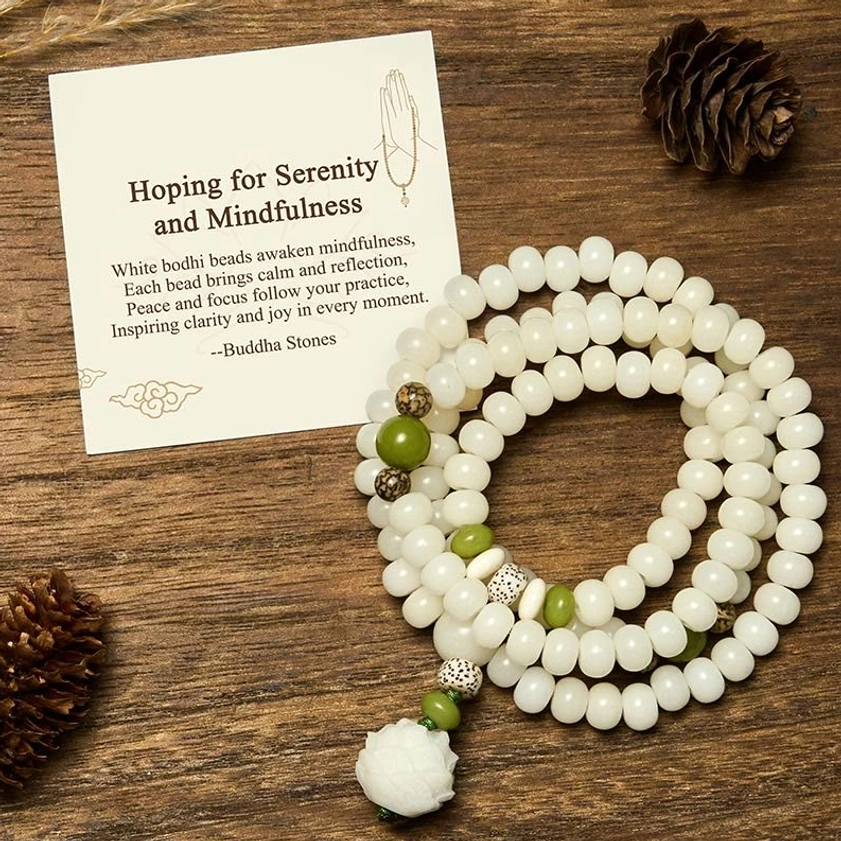 White Bodhi lotus mala beads with green accent beads and lotus pendant, overhead flat lay view on wooden surface