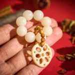 White bodhi seed lotus pendant meditation bracelet held in hand overhead view with dried flowers on red fabric background