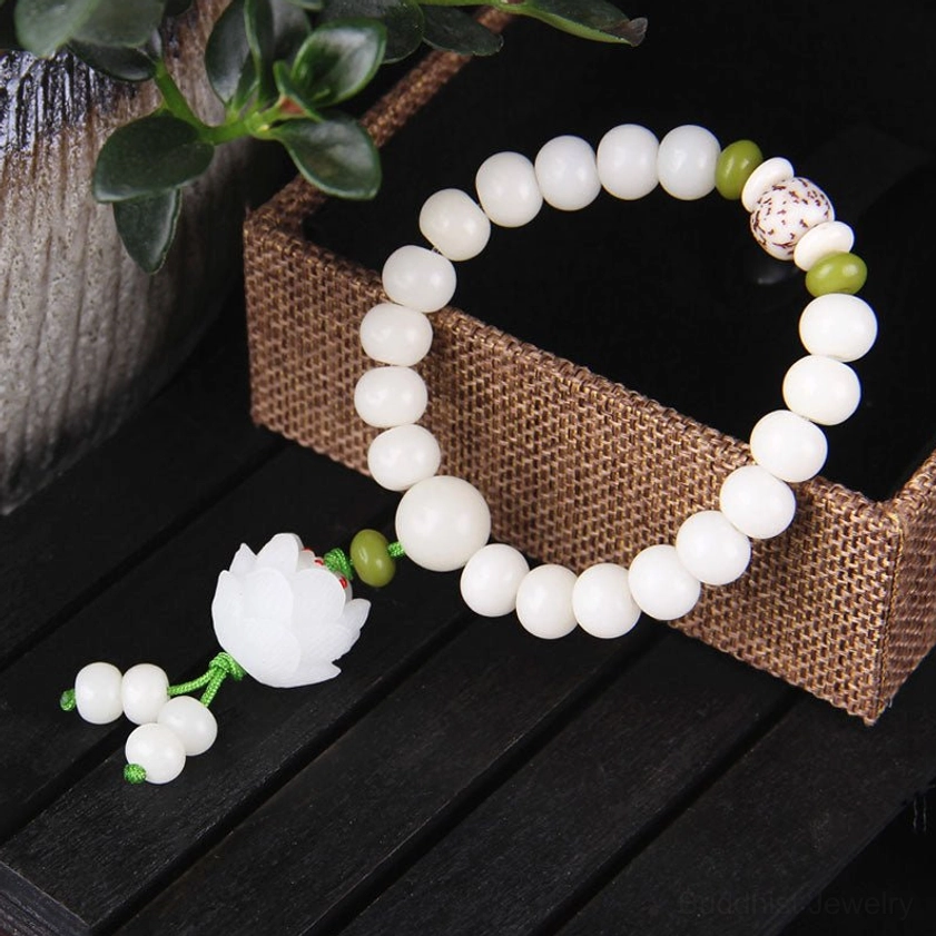 Polished white Bodhi seed bracelet three-quarter side view with green spacers, carved lotus bead tassel, and linen box on dark wood table background