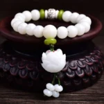 White Bodhi seed lucky bracelet with lotus pendant displayed on wooden stand, overhead front view showing matte white beads with green spacers and carved lotus tassel