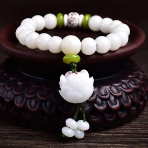 White Bodhi seed lucky bracelet with lotus pendant displayed on wooden stand, overhead front view showing matte white beads with green spacers and carved lotus tassel