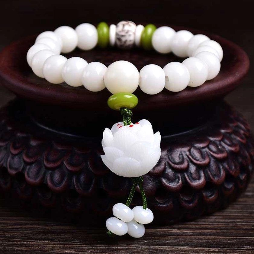 White Bodhi seed lucky bracelet with lotus pendant displayed on wooden stand, overhead front view showing matte white beads with green spacers and carved lotus tassel