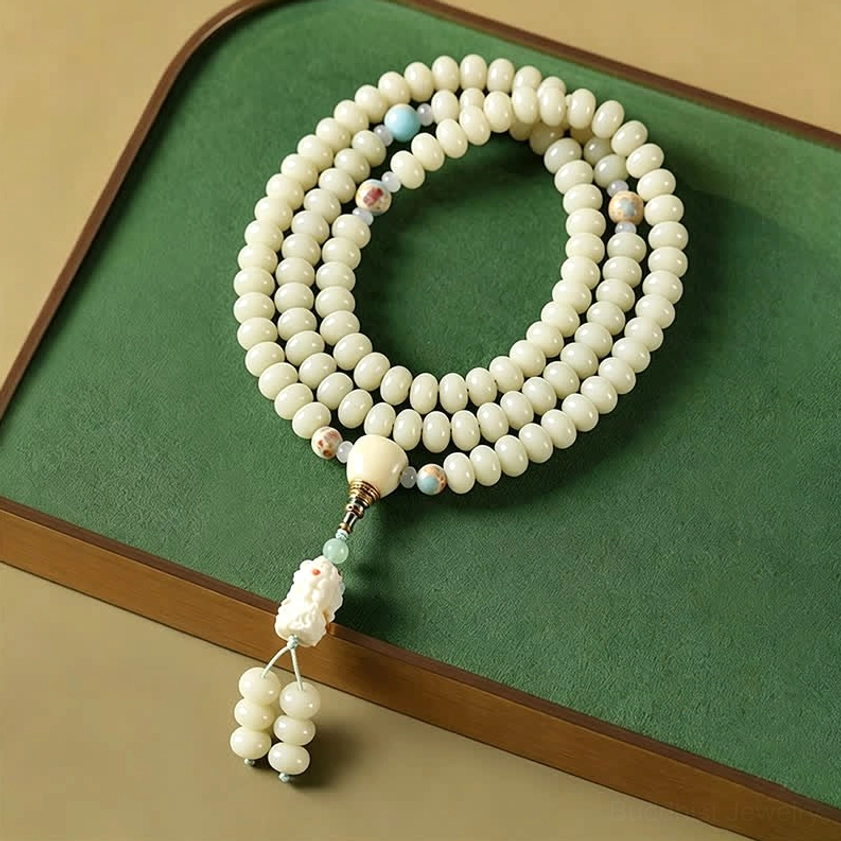 White bodhi seed 108 mala beads with carved Tara Bodhisattva pendant on green wooden tray, showing full prayer necklace length