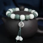 White bodhi seed six-word mantra protection bracelet with carved mantra beads, lotus pendant, and gourd tassel on dark background