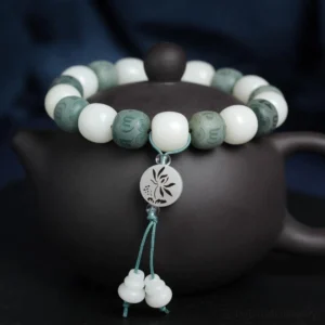 White bodhi seed six-word mantra protection bracelet with carved mantra beads, lotus pendant, and gourd tassel on dark background