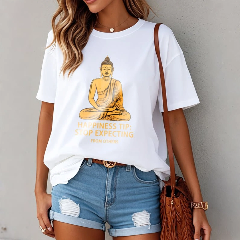 Female model wearing white Buddhist mindfulness t-shirt with golden Buddha graphic, casual styling with ripped denim and brown crossbody bag