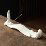 White ceramic Buddhist incense burner with monk and wave design on wooden tea table with incense stick