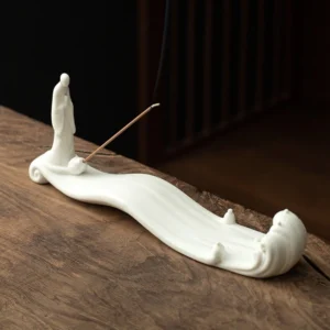 White ceramic Buddhist incense burner with monk and wave design on wooden tea table with incense stick