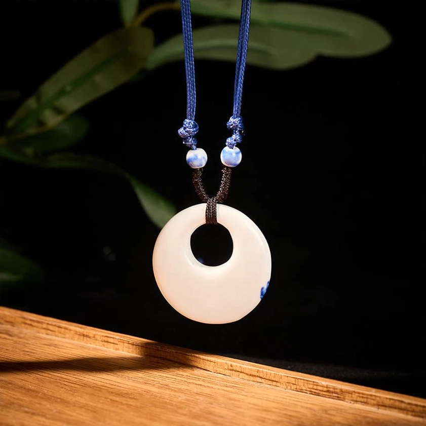 Plain white ceramic pendant necklace frontal hanging view with tiny blue spot detail on dark background