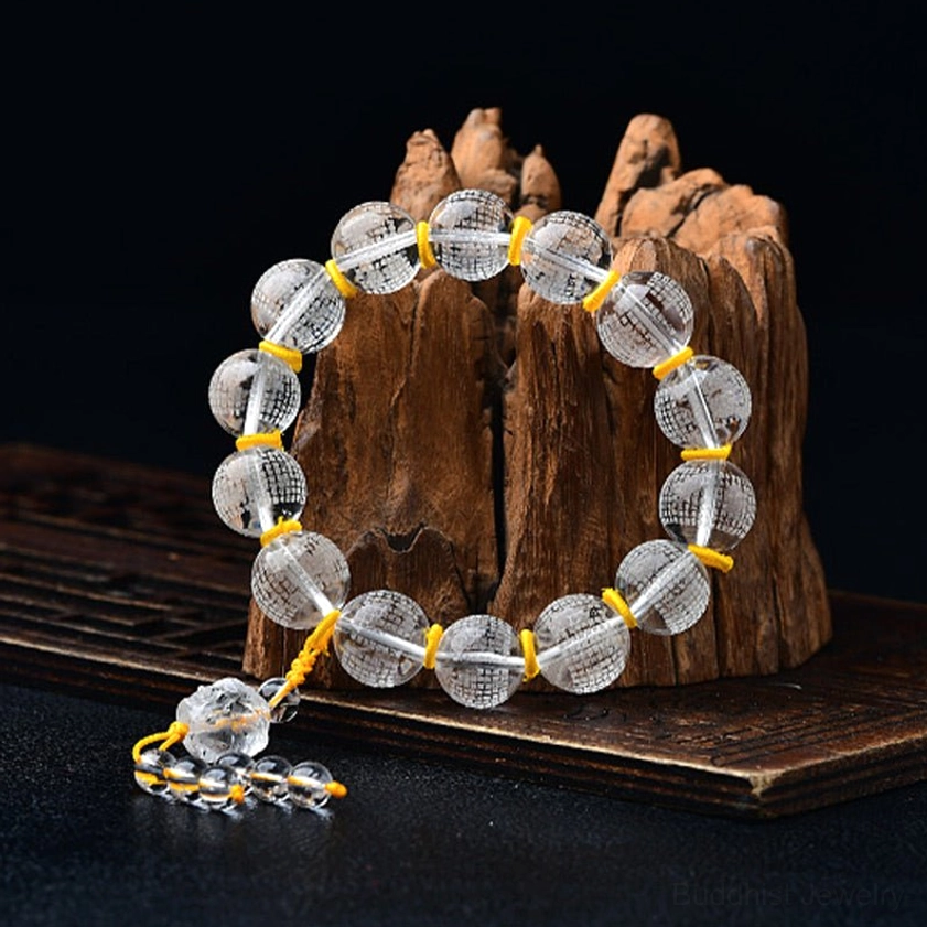 Single white crystal meditation bracelet on wooden stump display, showing three-quarter view with engraved Buddhist beads, yellow cord accents, and hanging crystal charm