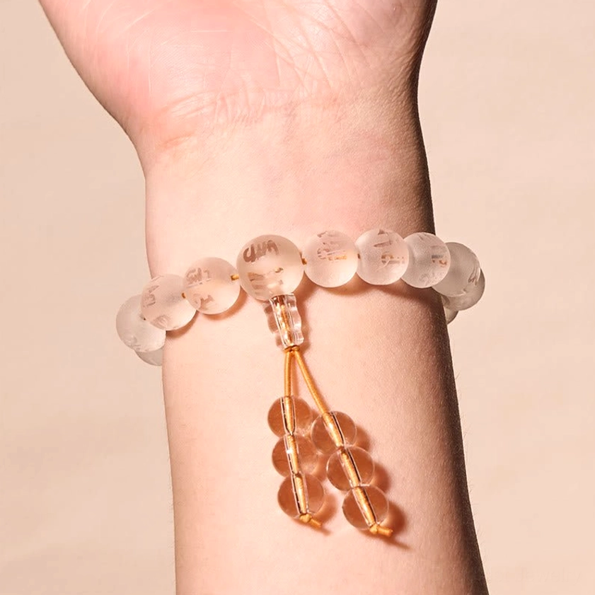 Frontal view of white crystal prayer bracelet on right human wrist displaying clear gemstone beads with golden decorative cord accents
