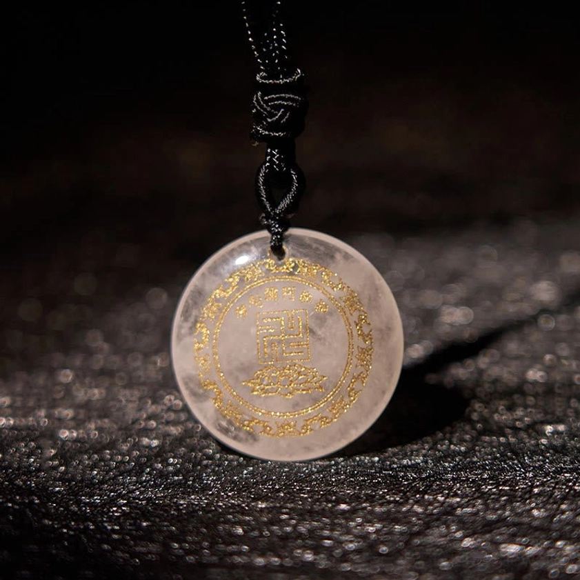 White clear quartz Buddhist pendant with gilded swastika lotus design and braided cord on leather background