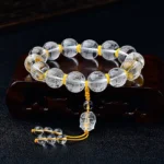 White crystal Heart Sutra bracelet with Half Demon Half Buddha charm engraved on clear beads, displayed on dark wooden stand with yellow nylon cord and crystal tassel