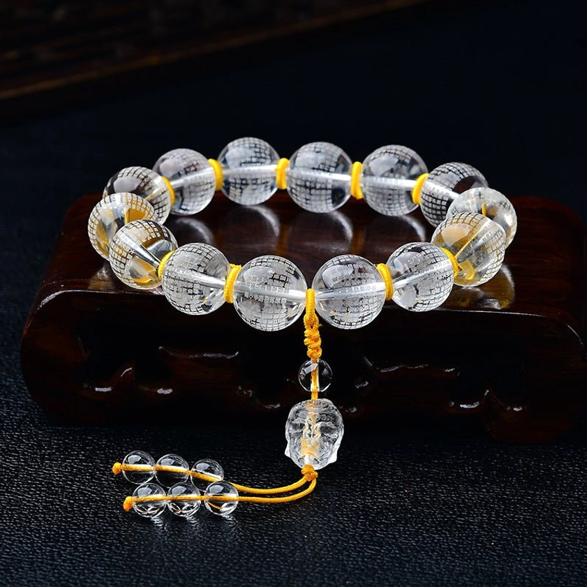 White crystal Heart Sutra bracelet with Half Demon Half Buddha charm engraved on clear beads, displayed on dark wooden stand with yellow nylon cord and crystal tassel