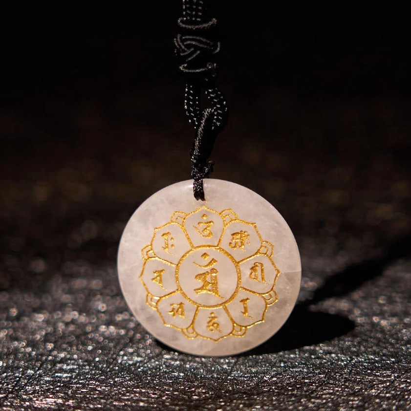 Clear Quartz White Crystal Om Mani Padme Hum Buddhist pendant with gold Sanskrit design on dark fabric background