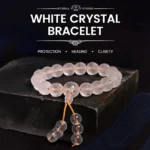 White Crystal Om Mani Padme Hum meditation bracelet with engraved sacred mantra beads and golden tassel cord, displayed on dark wooden stand