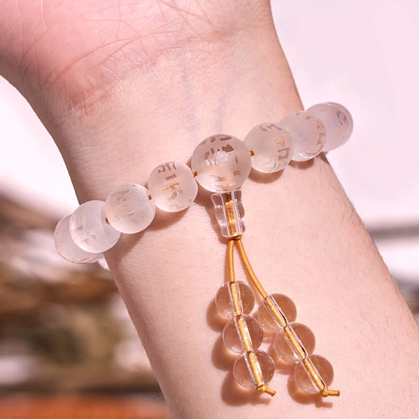 Clear crystal bracelet with golden tassel worn on wrist showing engraved mantra beads