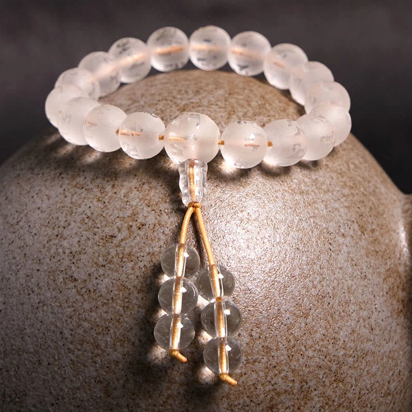 Clear white crystal mala prayer bracelet with engraved beads and golden cord on ceramic background