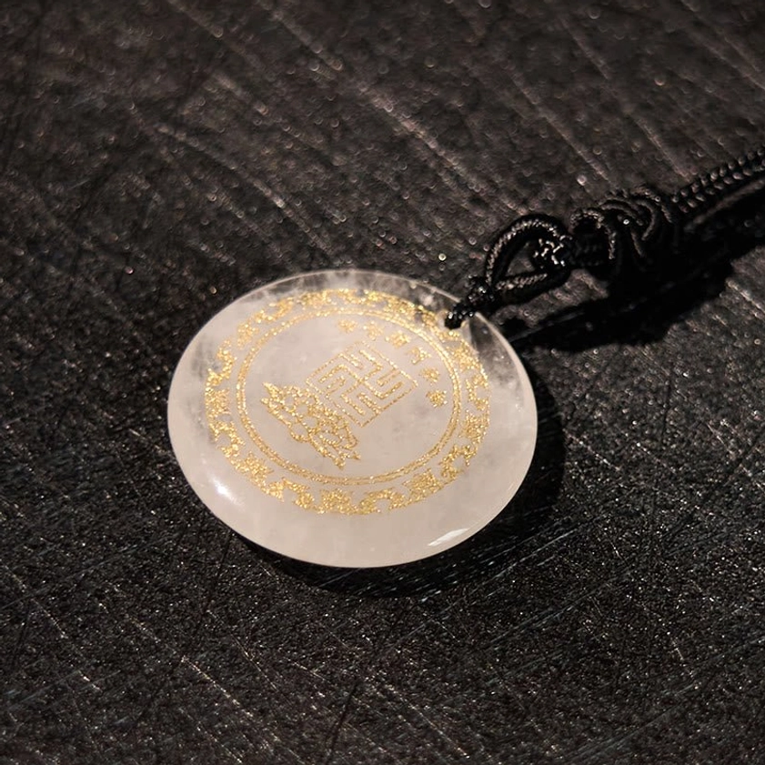 Clear quartz Buddhist pendant overhead close-up showing gold decorative border and lotus pattern