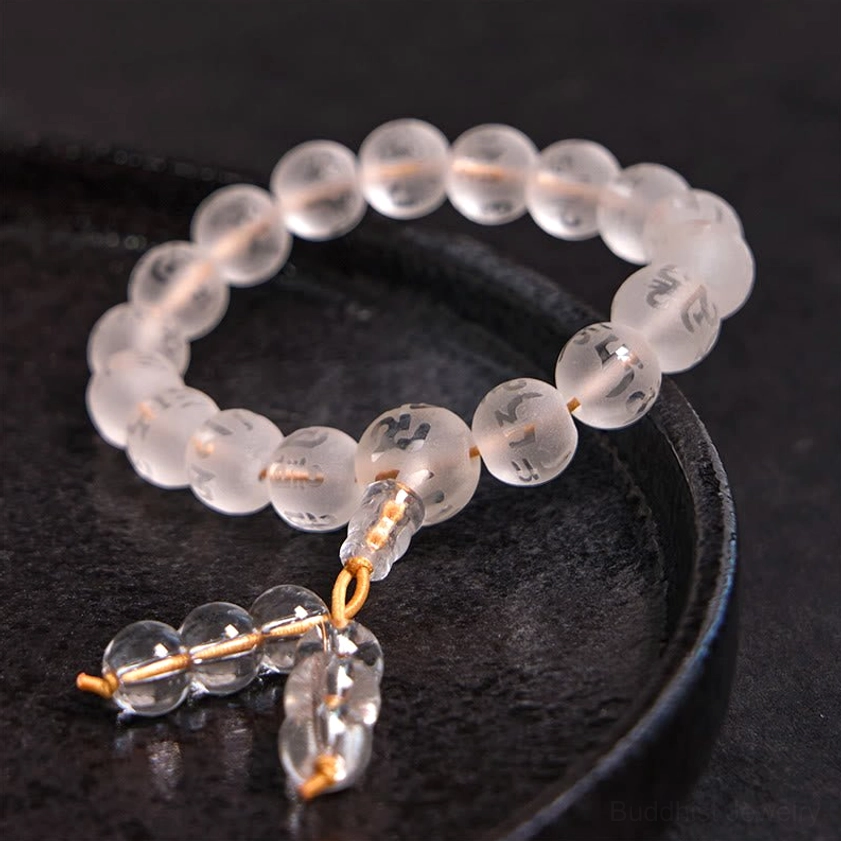 Close-up side view of white crystal prayer beads showing transparent round gemstones with hand-engraved sacred Sanskrit characters on black ceramic tray