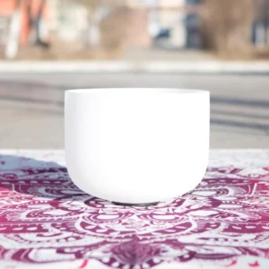 White crystal singing bowl handcrafted for meditation and chakra healing, displayed on mandala cloth with natural outdoor lighting